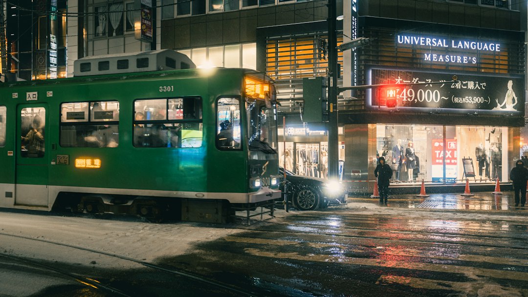 Green streetcar traveling through snowy Sapporo at night with city lights